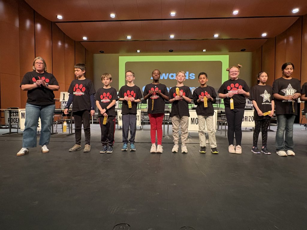 Group of young people standing on stage in front of microphones, smiling at camera, wearing black shirts with red and white