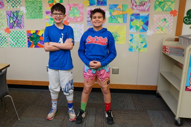 Students sitting at desks in a classroom, looking forward to the teacher who is standing at the front of the room.