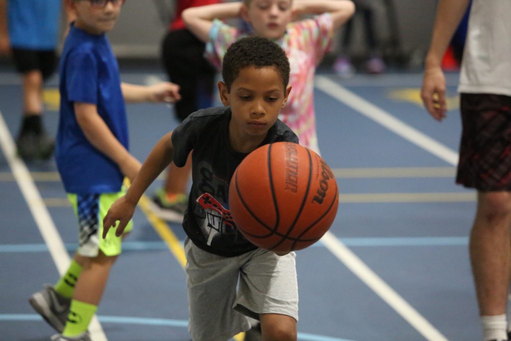 Boy in blue shirt dribbling basketball on court.